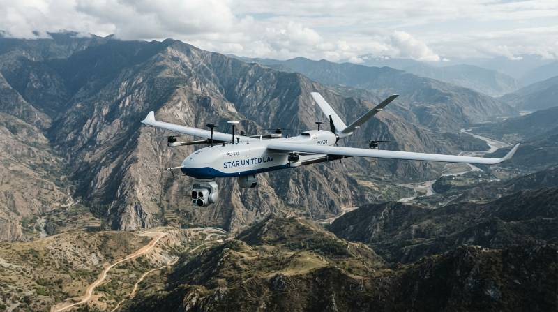 Industrial VTOL fixed-wing drone carrying multi-sensor gimbal flying above rugged terrain